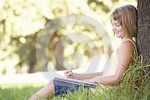 Young Girl Sketching In Countryside Leaning Against Tree