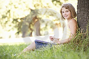 Young Girl Sketching In Countryside Leaning Against Tree