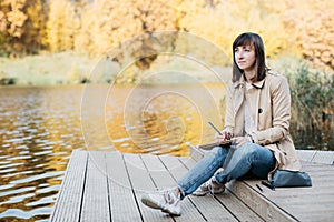 A young girl sketching near a lake in the autumn forest.