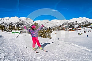 Young girl on a ski lifting her hands up in a cheer with ski resort and mountains in background, Andorra