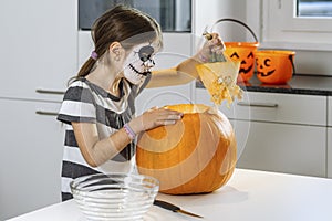 Young girl with skull face paint carving a pumpkin