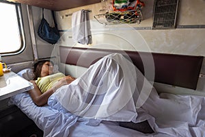 A young girl sleeps on a lower bunk in a reserved seat of a train car