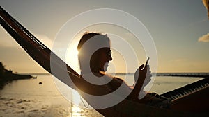 Young Girl with Smartphone in Hammock Silhuette Against Beautiful Sunset at the Beach. Koh Phangan, Thailand. HD