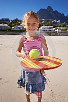 Young girl, smile and tennis ball in beach with bat, playing and active outdoor. Child, motor skills and growth for