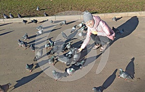 A young girl smiles and feeds a flock of gray pigeons on the street