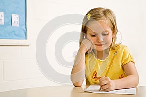 Young Girl Smiling in Classroom Writing on Paper