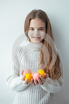 Young girl smiling holds easter colorful eggs white background sweater brown hair