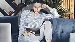 Young girl on sofa with digital tablet in her hand. Online communication via apps and messengers. Commenting and sharing in web