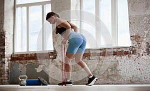 Young girl with sportive slim body training with fitness expanders indoors on daytime. Keeping body fit and strong