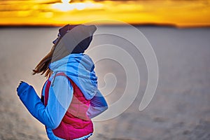 A young girl in a sports hat and jacket makes a morning jog on the embankment in the morning before the dawn of the sun.