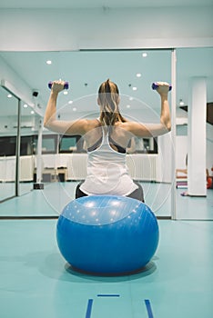 Young girl in sports suit does physical exercises with dumbells