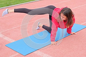 A young girl in sports uniform doing stretching on the blue rubber Mat at the stadium. Fitness classes in the fresh air.