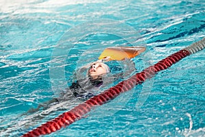 Young girl sportsman swiming backstroke with kickboard in pool