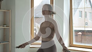 Young girl in sportswear does jump exercise in bright room with skipping rope