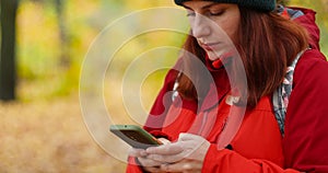 Young girl in sportswear uses a smartphone, writes SMS in the park. Autumn season trip