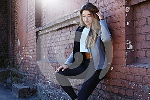 Young girl in a sportwear is exercising in front of the urban red brick wall. Phot was made on a sunny morning.