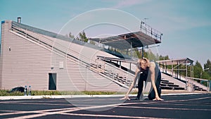 Young girl, sporty physique, at the stadium. She goes to the start line, gets into a low start