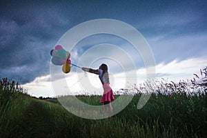 Young girl staing with balloons at the field during the storm