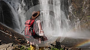 young girl standing with backpack observing a forest landscape with waterfall. Active turism norway