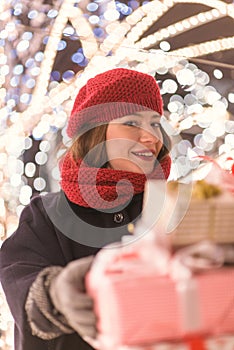 Young girl standing in front of Christmas tree lights hiding behind presents alone in the park