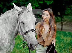 Young girl standing with a grey horse on a grass. Learn horseback riding through lessons. Explore horse therapy, hippotherapy. A