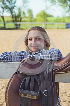 Young Girl Standing In The Horse Ranch - A Saddle Hanging On The Wooden Fence