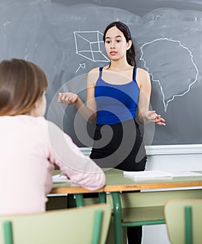 Young girl is standing near blackboard and writing solution of the homework in the classroom