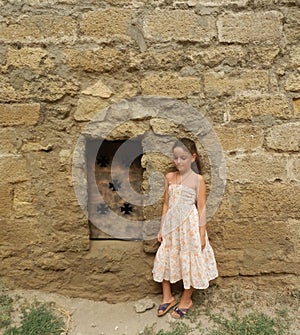 A young girl standing near medieval metal door in the limestone wall