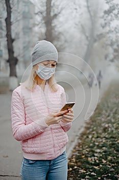 A young girl is standing near the road in a medical mask. Protection against a virus epidemic in a city.