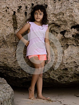 Young girl standing near the rock. Happy childhood. Spending time on the beach. Girl wearing shorts. Vacation in Asia. Pandawa