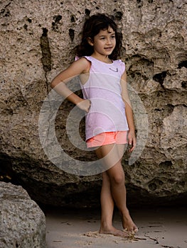 Young girl standing near the rock. Happy childhood. Spending time on the beach. Girl wearing shorts. Vacation in Asia. Pandawa