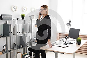 A young girl standing in the office and talking on the phone.