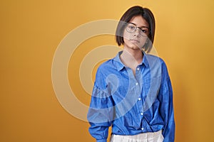 Young girl standing over yellow background relaxed with serious expression on face