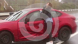 A young girl standing in the rain on an empty road near her broken car.