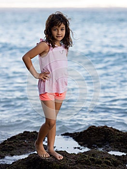 Young girl standing on the rock near the ocean enjoying nature. Happy childhood. Spending time on the beach. Vacation in Asia.