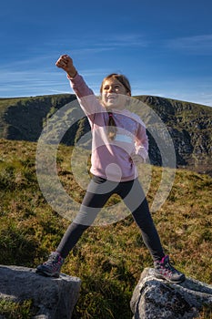 Young girl standing on two rocks with raised hand in triumph as she climbed mountain, Wicklow, Ireland