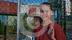 Young girl stands with ball on football field and looks into distance through net closeup