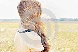 Young girl stands in the field and wind flutters her hair
