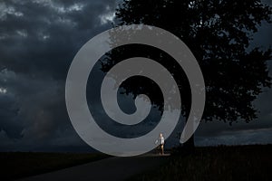 Young girl stands with her longboard in the middle of the road next to a big tree