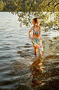 Young girl stands knee-deep in the water of a river and squeezes a wet dress