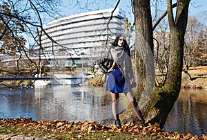 Young girl stands near river in city park on autumn day