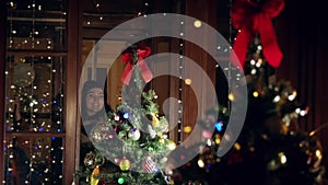 A young girl stands outside the window and looks at a beautiful Christmas tree through the glass. Christmas mood