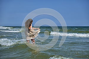 Young girl stands in the sea, lifting the edge of a sundress so that it would not be wet