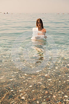 A young girl stands waist-deep in sea water and looks at the camera lens