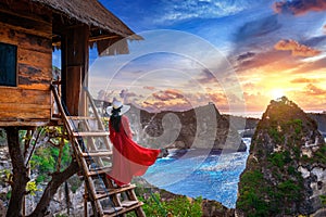 Young girl on steps of house on tree at sunrise in Nusa Penida island, Bali in Indonesia