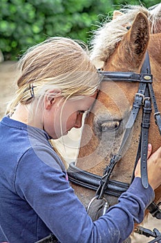 A young girl strokes her pony and speaks sweet words to the horse.