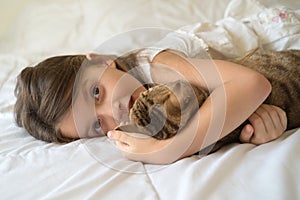 Young girl stroking cat lying on bed