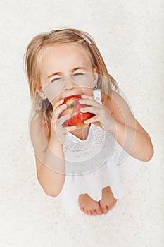 Young girl struggling to take a large bite of apple