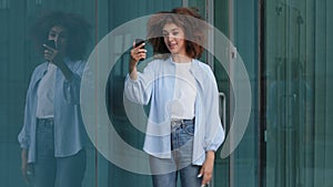 Young girl student african american woman with curly hair standing outdoors in city answers video call waving hello