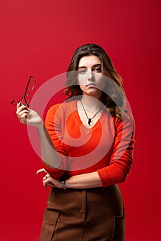 Young girl student or business woman girl with skeptic expression took off glasses on a red background